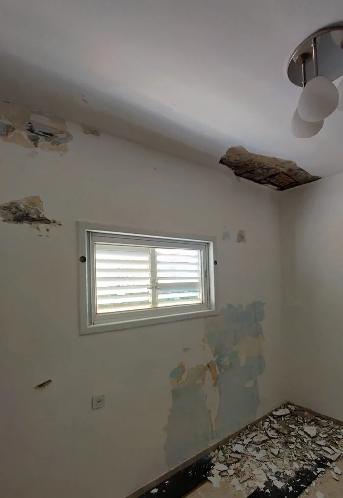 קיר ותקרה בחדר עם אזורים מתקלפים וטיח חשוף לפני התיקון