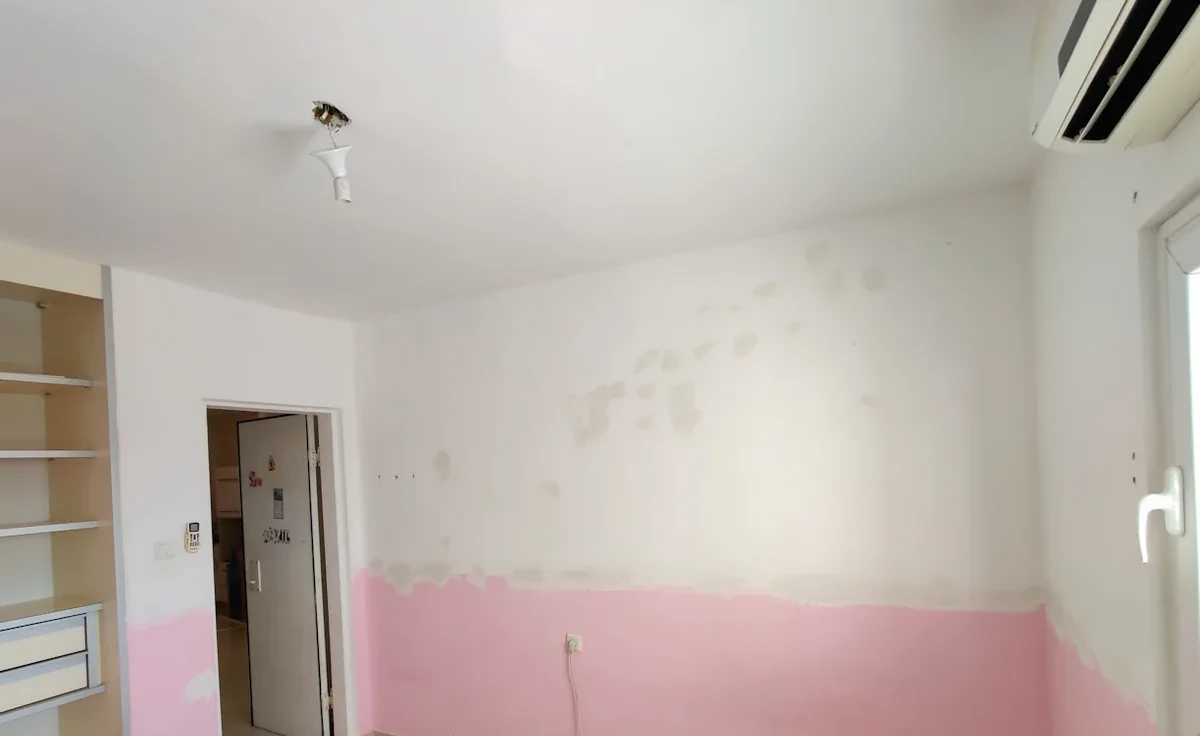 חדר עם קיר ורוד בחלקו התחתון וסימני תיקון לפני הצביעה
