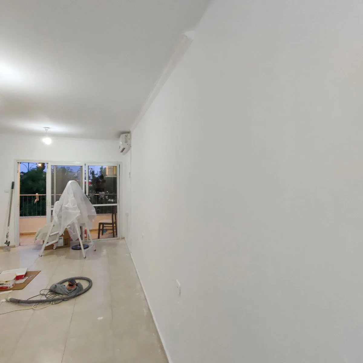 הכנת קירות בחדר גדול עם רהיטים מכוסים ומכשיר שיוף עם שואב אבק